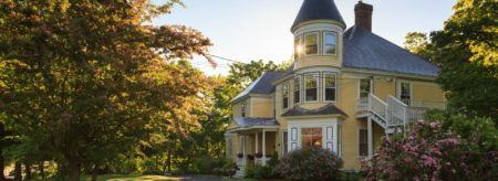 Exterior view of the property painted light yellow with white trim surrounded by large green lawn and large green trees