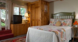Bedroom with white walls, built-in wooden closet, white bedding, multicolored blanket and pillows, and TV