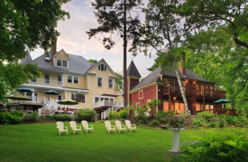 Exterior view of the property painted light yellow with white trim surrounded by large green lawn and large green trees