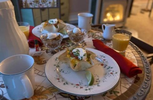 Small table with two place settings containing an egg breakfast dish in a baked tortilla, fruit crumble, and orange juice