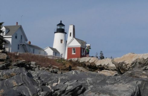 View of a white house, white lighthouse, and small red building near large rocks