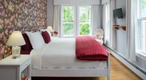 Bedroom with white walls, floral wallpaper, white bed, white bedding, red blanket, and flat-screen TV
