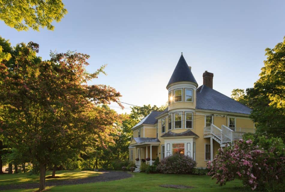 Front exterior view of the property painted light yellow with white trim and surrounded by green grass and large trees