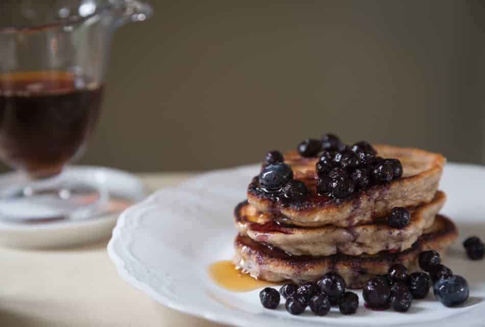 White porcelain plate with a stack of pancakes covered in syrup and blueberries